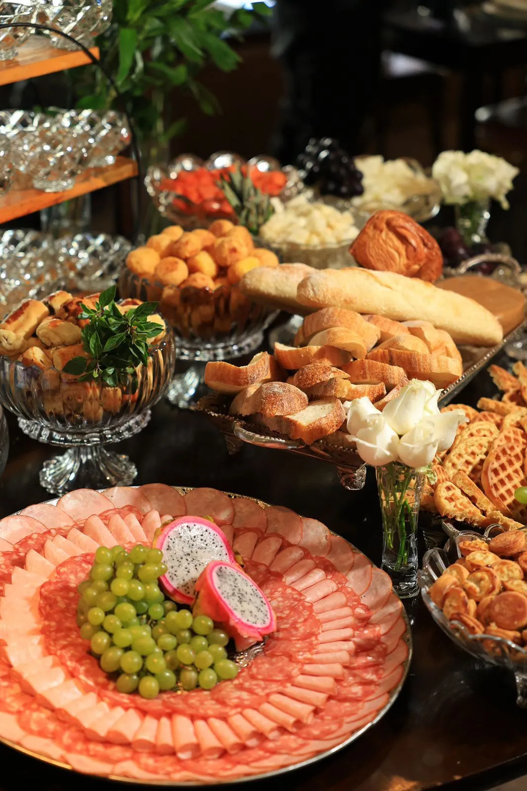 Travessa de frios com uvas e pitaya, pães e taças de cristal