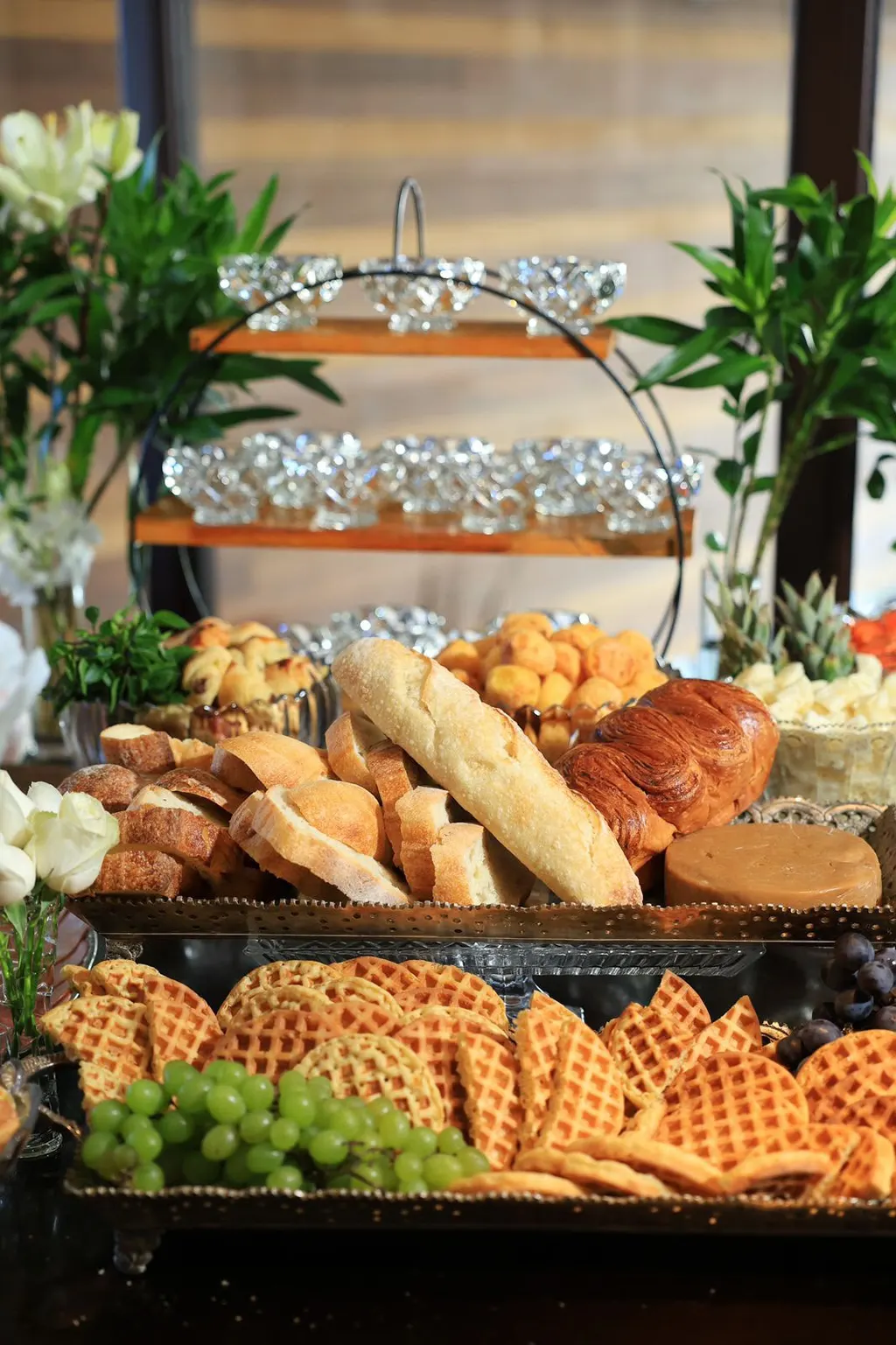 Pães, croissant e waffles em bandeja de prata com uvas verdes