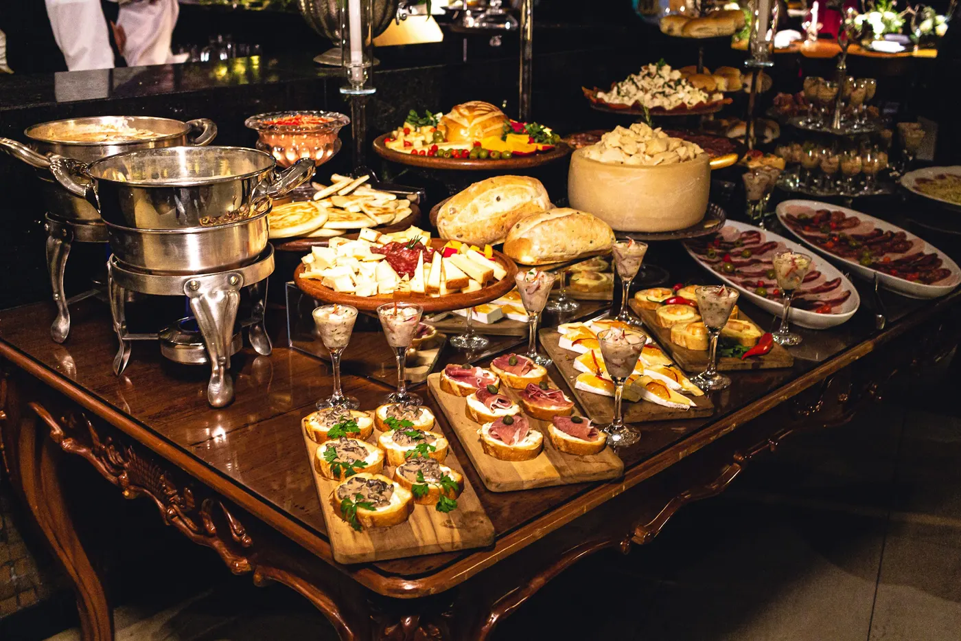 Mesa de jantar noturno com queijos, pães, canapés e réchauds