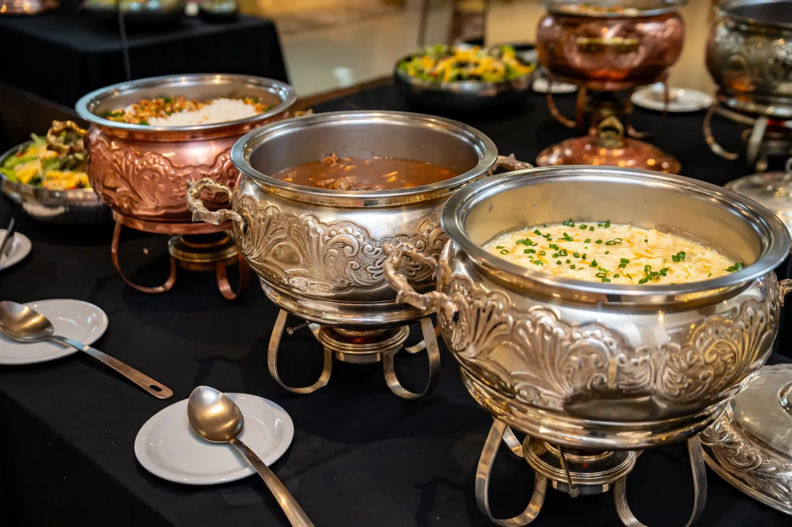 Réchauds de prata e cobre com pratos quentes em mesa de almoço corporativo